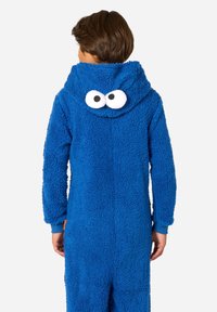 Modra puhasta enodelna obleka s kapuco, na hrbtni strani pa so velike bele risane oči. Elastične manšete in stranski žepi. Mehka, teksturirana tkanina.