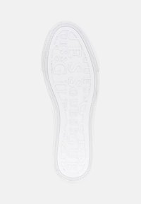 Vitt skosole med det upphöjda varumärkesnamnet "GUESS" upprepat i mönstret på en enkel vit bakgrund.