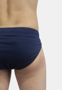 Costume da bagno slip blu navy con una texture liscia, vita elastica e design aderente, che offre una copertura completa sul retro.