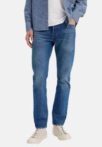 Vaqueros de mezclilla azul claro con un diseño de pierna recta, estilo de cinco bolsillos y un ligero desgaste. Llevados con zapatillas blancas.