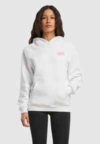 Sudadera blanca con capucha y un texto "LOVE" en rosa en la parte izquierda del pecho. Presenta un bolsillo frontal y puños de canalé. Tela de textura suave.