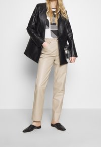 Black leather blazer over a white top with striped pattern, beige leather trousers, and black slip-on shoes with a textured finish.