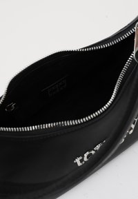 Sac noir avec fermeture éclair, présentant une texture mate lisse et des accessoires en métal argenté. À l'intérieur, doublé d'un tissu sombre, avec une étiquette visible.