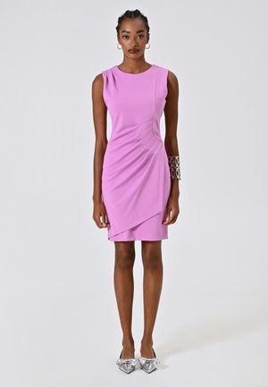 Robe sans manches fuchsia avec un design drapé et des plis à l'avant. Le mannequin porte des chaussures plates argentées avec un détail en nœud et un bracelet en métal.