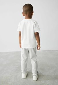 Valkoinen lyhythihainen t-paita yhdistettynä vaaleanharmaisiin, teksturoiduista materiaaleista valmistettuihin verkkareihin ja valkoisiin lenkkareihin, joissa mustia yksityiskohtia ja kantapäässä sana "BAKER".