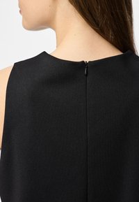 Juodas be rankovių suknelė su apvaliu iškirpimu ir uždara užtrauktuko uždarymu gale. Audinys turi lygų, matinį paviršių.