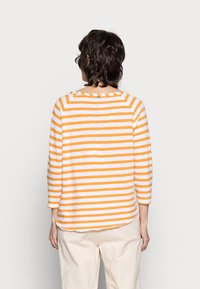 Gestreiftes Langarmshirt mit abwechselnden orange- und weißen Streifen, Rundhalsausschnitt und leicht abgerundetem Saum. Baumwollmaterial.