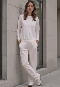 Witte lange mouwen top en bijpassende joggers, beide gemaakt van een zachte stof. Subtiele textuurafwerking, met een klein logo detail op de tailleband.