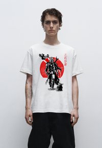 Bílý bavlněný tričko s černým a červeným grafickým potiskem postavy a malé postavičky, s japonským textem na přední straně.