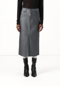 Jupe midi en denim gris avec fente avant, cinq poches et passants de ceinture. Associée à des bottines noires et un haut noir à manches longues texturé.