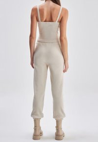 Beige pruhovaný crop top s tenkými ramínky spárovaný s odpovídajícími zúženými tepláky. Obsahuje měkkou texturu a elastický pas, doplněný kotníkovými botami.