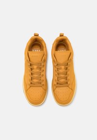 Baskets en cuir jaune avec une texture lisse, dotées de perforations, de lacets plats et d'une doublure intérieure douce. La semelle est blanche avec une légère courbe.