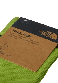Gröna strumpor för herr i paket med en brun pappersetikett. Etiketten visar produktnamnet "Trail Run" och storlek "M" i svart text.