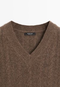 Brauner Strickpullover mit V-Ausschnitt und Zopfmuster. Etikett innen am Kragen sichtbar. Weiche Textur und gerippte Kanten verfeinern das Design.