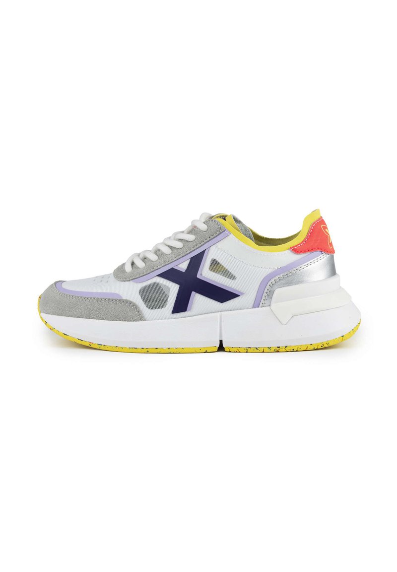 Baskets de sport en blanc, gris et violet. Elles présentent un dessus texturé, des accents jaunes, et une épaisse semelle blanche avec un design moucheté.