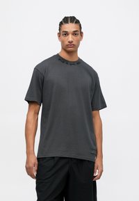 Camiseta de algodón gris oscuro con mangas cortas, cuello redondo y logotipo en relieve en negro de "NIKE" en el frente. Acompañada de pantalones cortos negros.