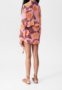 Short-sleeve, tie-dye dress in pink, orange, and brown hues, with a relaxed fit and slightly cropped back, paired with tan strappy sandals.