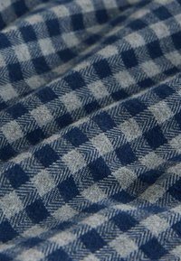 Geweven stof met een blauw en grijs geruit patroon met afwisselende vierkanten en visgraataccenten, met een zachte, gestructureerde oppervlakte.