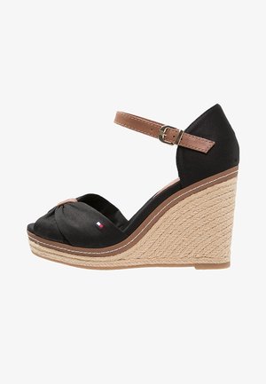 Czarne sandały na koturnie z plecioną podeszwą, brązowy pasek na kostkę z klamrą oraz zawiązany front z tkaniny z małym detalem w postaci flagi.