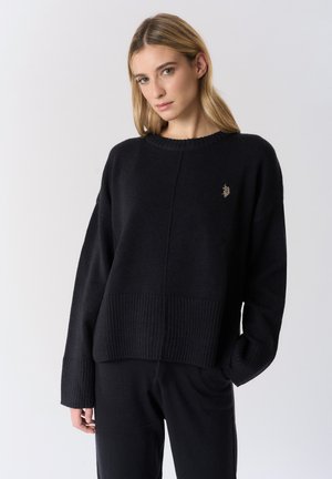 Maglione nero lavorato a maglia con orlo e polsini a coste. Presenta una scollatura rotonda e un dettagliato logo discreto sul petto. Vestibilità casual e rilassata.