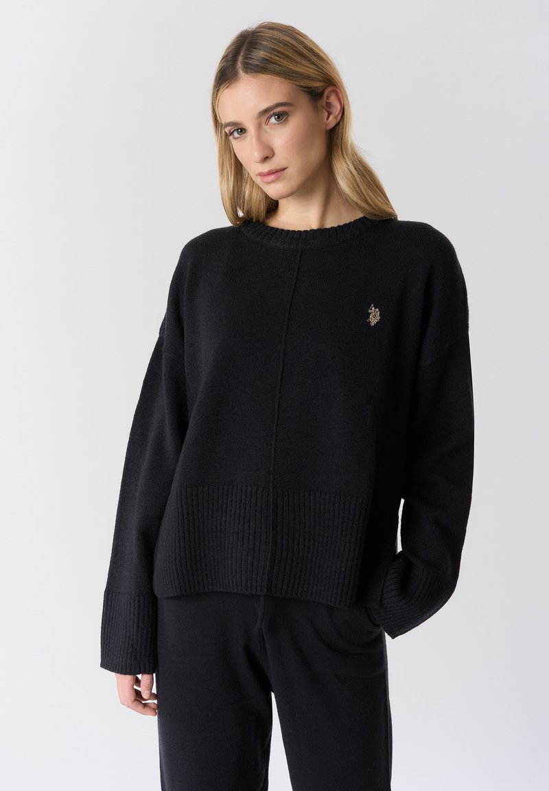 Maglione nero lavorato a maglia con orlo e polsini a coste. Presenta una scollatura rotonda e un dettagliato logo discreto sul petto. Vestibilità casual e rilassata.