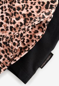 Tkanina s uzorkom leopardovih pjega u nijansama smeđe i crne složena preko jednobojne crne tkanine; sadrži detalje šavova i etiketu na kojoj piše "ROCKETT GEORGE."