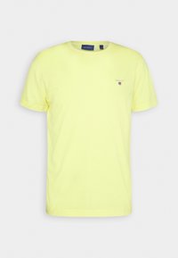 T-shirt en coton jaune à manches courtes, avec un col rond et un petit logo brodé sur la poitrine. Texture douce et coupe classique.
