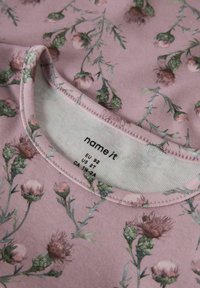 Hellrosa Hemd mit Distel-Blumenmuster, ausgestattet mit einem runden Ausschnitt und weichem, dehnbarem Stoff. Pflegeetikett am Kragen sichtbar.