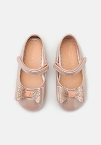 Jasnoróżowe lakierowane buty typu Mary Jane z ozdobną błyszczącą kokardą i regulowanym paskiem, charakteryzujące się gładką, błyszczącą powierzchnią.