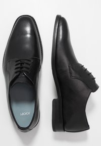 Scarpe eleganti in pelle nera con una finitura liscia, dotate di chiusura con lacci e punta arrotondata. Suola texturizzata con tacco basso.