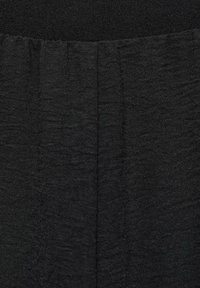 Black fabric with a textured finish, featuring a gathered pleat design at the lower section and a smooth waistband at the top.