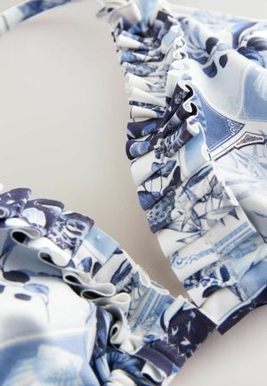 Bikini top with ruffled edges, featuring a blue and white pattern with floral and scenic designs, made from stretchy fabric.