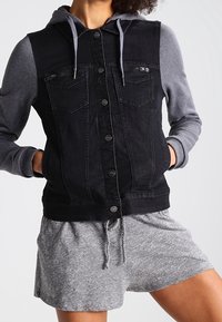 Svart jeansväst med en grå hoodie, i en design med knäppning, dubbla bröstfickor och grå shorts. Mjuk textur och avslappnad design.