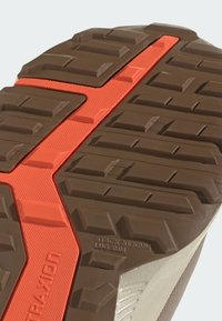 Trailrunning-Schuhsohle mit tiefen Profilen; braunes Gummi-Material mit einem orangefarbenen Streifen für besseren Halt. Auffällige strukturierte Muster sorgen für Grip.