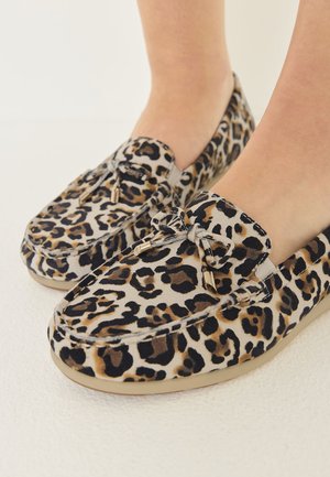 Pies con mocasines de estampado de leopardo con un lazo y terminales metálicos sobre un fondo claro.