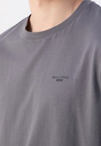 Camiseta de algodón gris con cuello redondo y mangas cortas, con un logo impreso sutil "Marc O'Polo DENIM" en el pecho izquierdo.