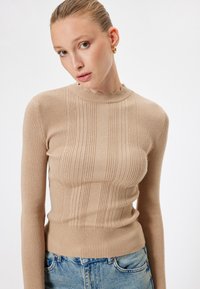Pullover beige a maniche lunghe con righe in rilievo, dal collo scallop e dettagli a strisce verticali; morbido al tatto con silhouette aderente.