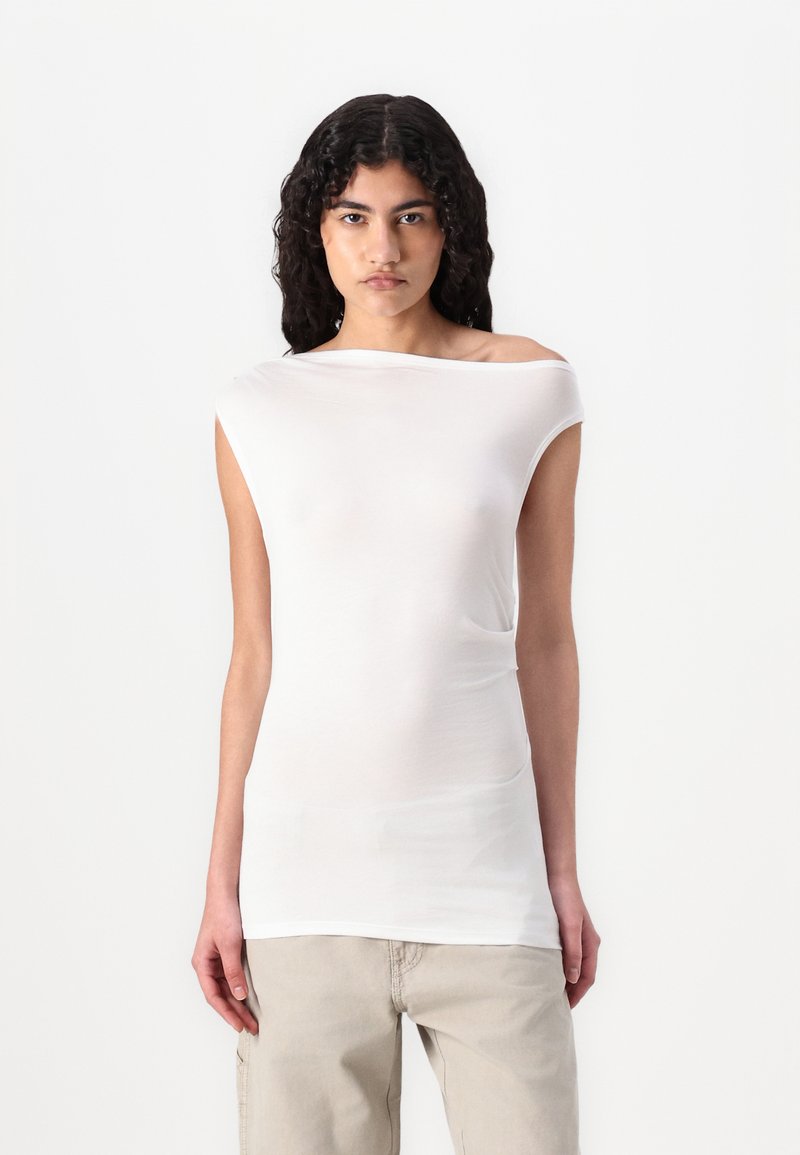 Haut blanc à manches courtes avec un col asymétrique, fabriqué en tissu léger et doux. Texture lisse, design ajusté et style minimaliste.