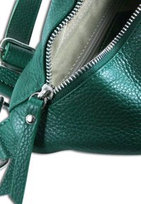 Groene leren handtas met een gestructureerd oppervlak, ritssluiting en zilverkleurige metalen details. Het interieur is gevoerd met een lichtgekleurde stof.