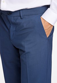 Navyblaue Hose aus glattem Stoff, mit geradem Schnitt, seitlichen Taschen und flachem Frontdesign mit einem einzigen Knopfverschluss.