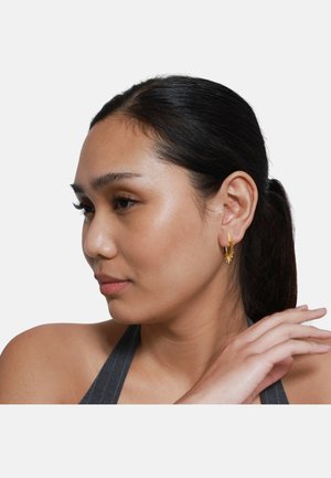 Boucles d'oreilles en or avec un design en éclat de soleil ; texture lisse ; attachées à une fine créole ; modèle montré de côté sur fond blanc.