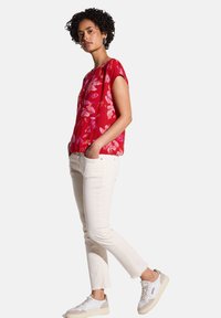 Blusa a fantasia floreale rossa con maniche corte, abbinata a jeans bianchi a sigaretta e sneakers con dettagli beige. Tessuto morbido.