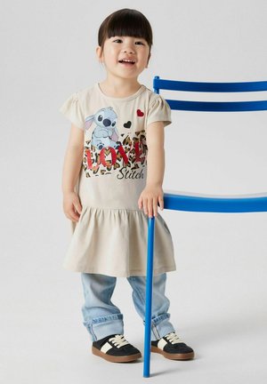 Valkoinen beige mekko, jossa on liehuva hame, edessä on Stitch-kuva ja "LOVE" punaisena. Yhdistetty sinisiin farkkuihin ja mustiin kenkiin.