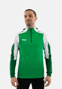 Maglia sportiva verde con zip e dettagli bianchi, caratterizzata da un collo alto, tasche laterali e logo sul petto e sulla cintura.