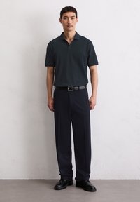 Marineblauw poloshirt met een klassieke kraag en korte mouwen, gecombineerd met donkergekleurde broeken en zwarte schoenen. Soepele stof en slim fit.