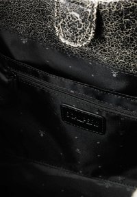 Interior de un bolso de mano de cuero negro agrietado con un forro de tela suave y negra. Cuenta con un bolsillo con cremallera y una etiqueta de la marca.