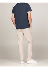 Granatowa koszulka z krótkim rękawem w połączeniu z jasnobeżowymi, dopasowanymi spodniami i białymi trampkami, wyróżniająca się prostym wzorem i miękką teksturą materiału.