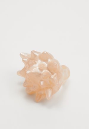 Plump, peach-colored ring featuring a textured, spiky design with a glossy finish. Made from a smooth, synthetic material.
