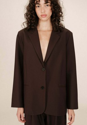 Blazer marron ajusté avec une finition mate, doté d'une fermeture à un bouton, de larges revers et d'une coupe décontractée avec des poches avant.