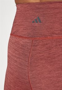 Leggings taille haute en rouge marbré avec une texture lisse, présentant un accent de logo sombre et des détails cousus le long des coutures.